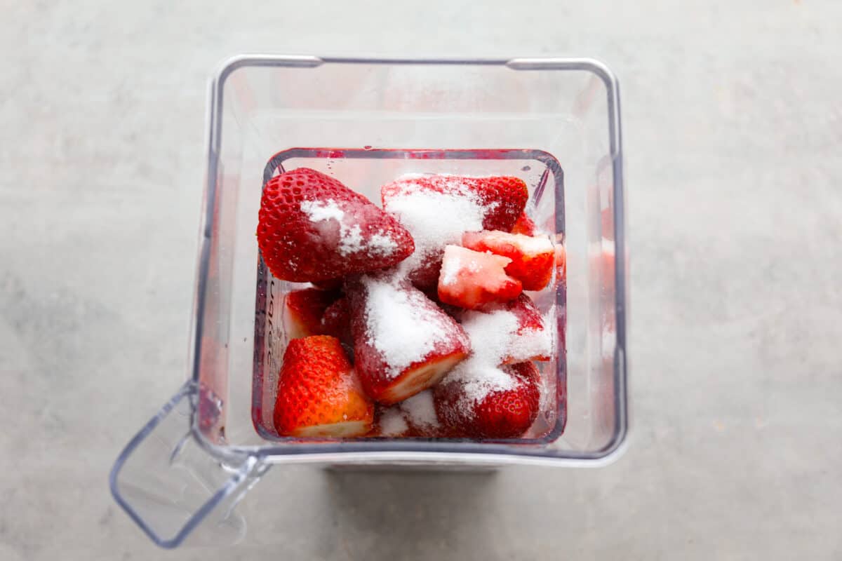 Elevate the flavors of traditional horchata with this strawberry horchata recipe! It's a creamy drink soaked in rice water and cinnamon sticks, then sweetened with a strawberry puree. Everyone loves the strawberry version of this rich, milky Mexican drink! Process photo of the strawberries, sugar, and lemon juice added to a blender.