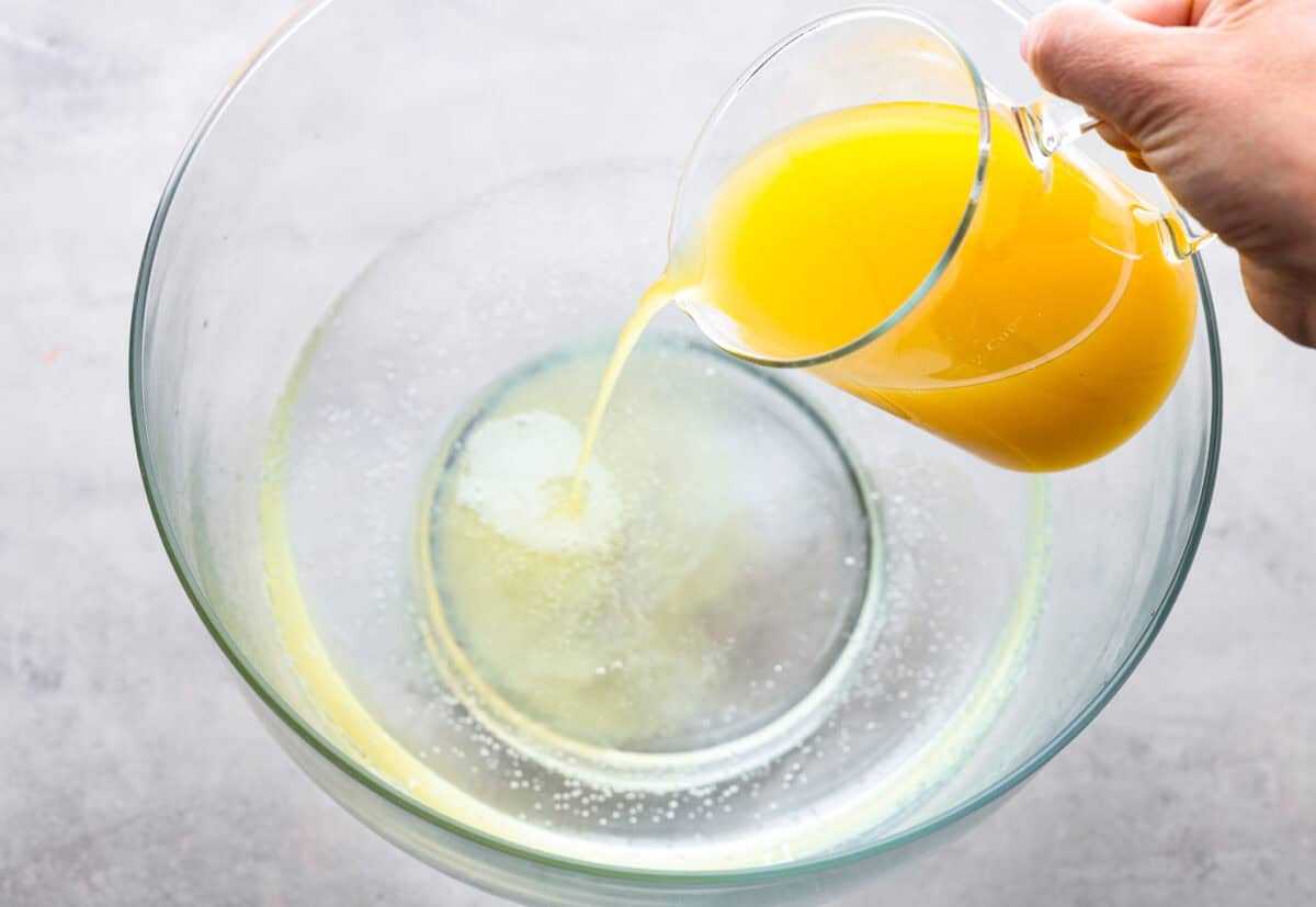 This bright sherbet punch is the perfect addition to any BBQ or gathering. Your guests will keep coming back for more and beg you for the recipe! It has just the right balance of sweetness, zest, and refreshing coolness, you'll be sure to beat the heat on a hot summer day. Overhead shot of pineapple juice being poured into a large bowl that already has Sprite in it.