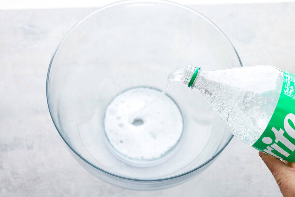 This bright sherbet punch is the perfect addition to any BBQ or gathering. Your guests will keep coming back for more and beg you for the recipe! It has just the right balance of sweetness, zest, and refreshing coolness, you'll be sure to beat the heat on a hot summer day. Overhead shot of sprite being poured into a large bowl.