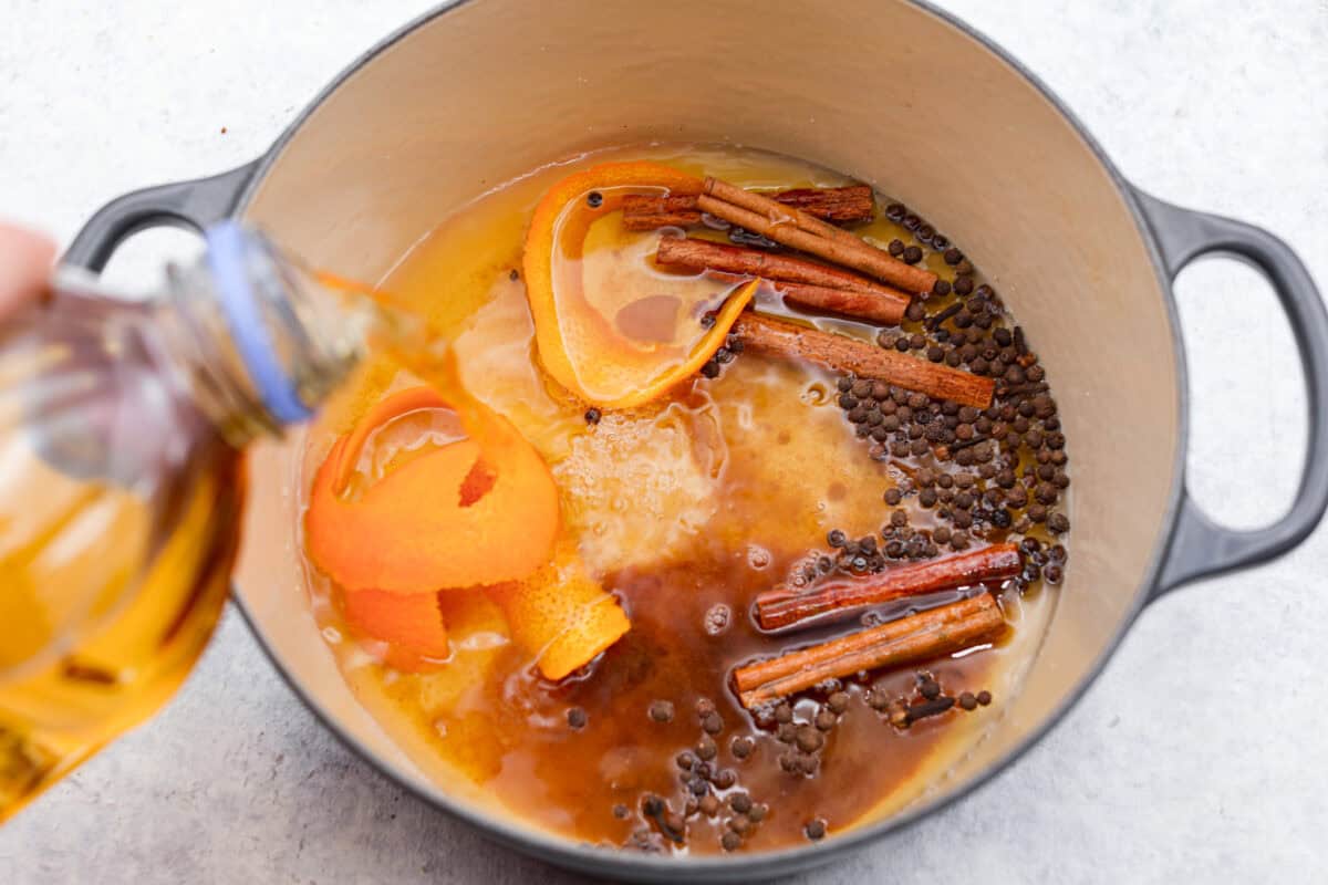 Mulled cider is a warm, inviting drink that is mixed with citrus and spices. Take your apple cider game up a notch with this easy recipe. Your house will smell amazing as well! Overhead shot of ingredients in the pot while someone pours apple cider over the top.