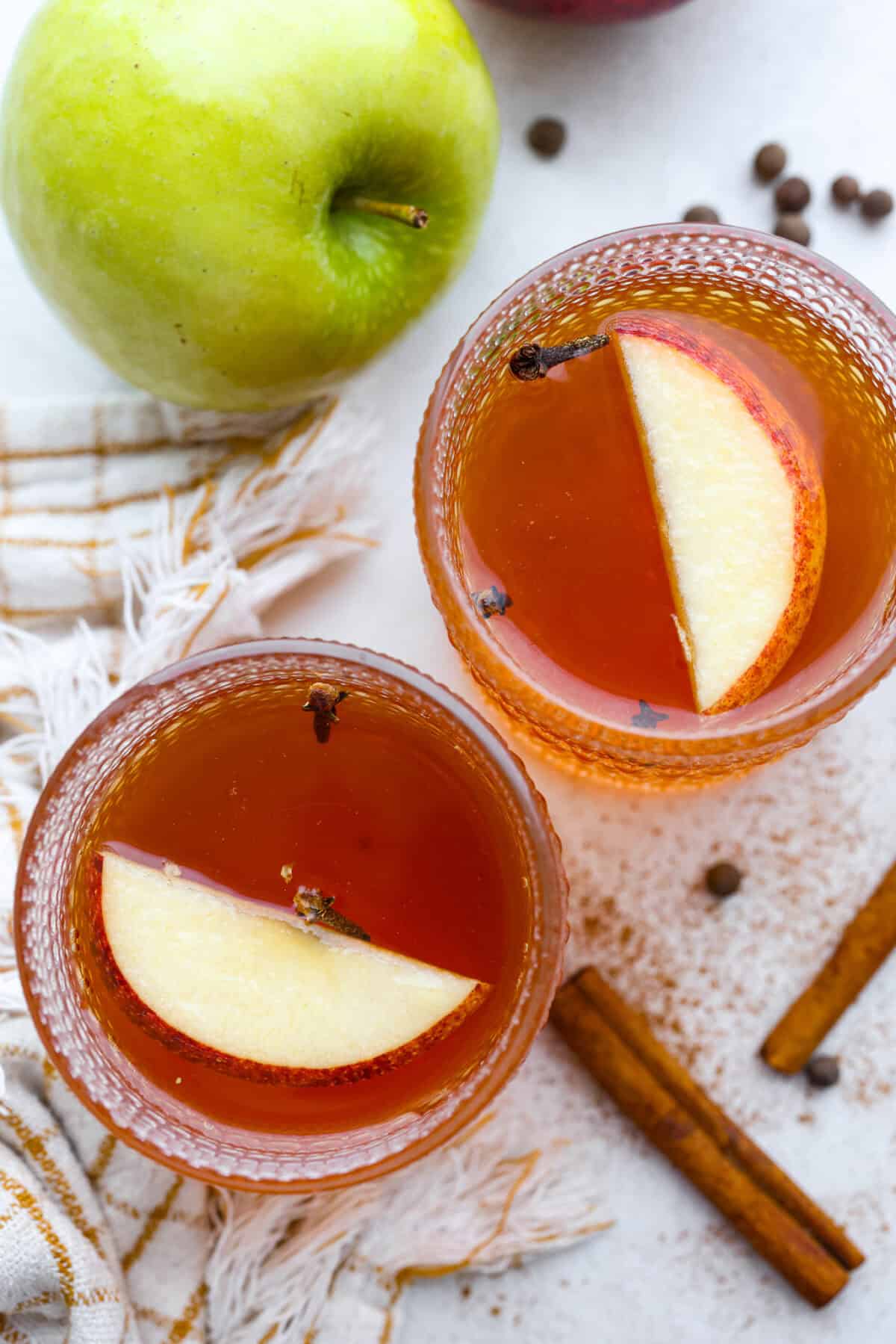 Mulled cider is a warm, inviting drink that is mixed with citrus and spices. Take your apple cider game up a notch with this easy recipe. Your house will smell amazing as well! Overhead shot of two glasses with mulled cider in them.